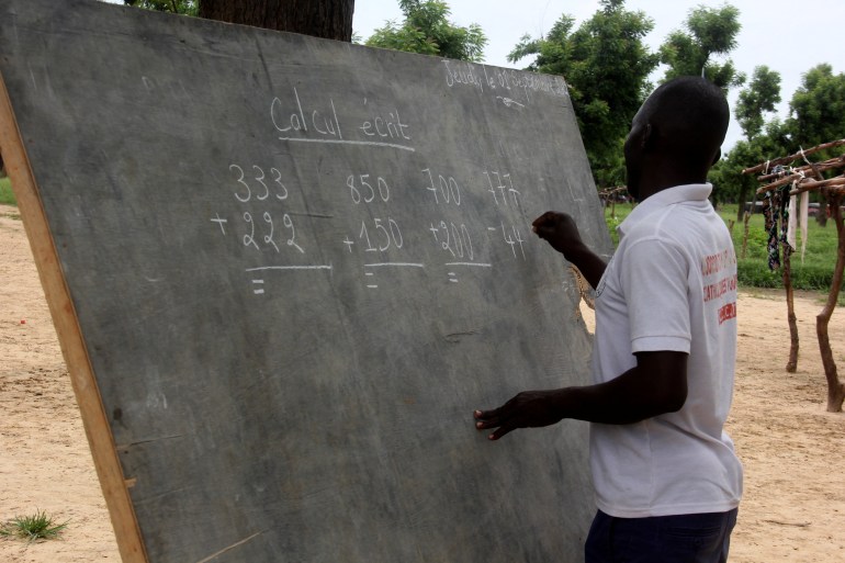 Leonard Gamaigue stands at a blackboard, we can see his profile and the sums he is writing on the board
